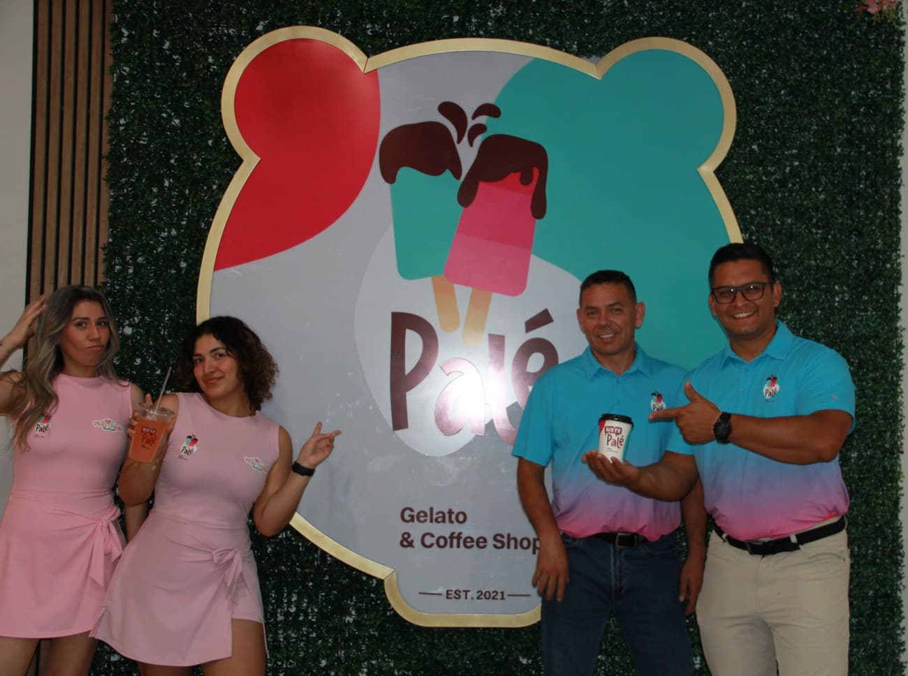 The Palé team, four people in pink and teal Palé shirts, posed in front of the bear-shaped Palé logo wall, one holding a Palé cup