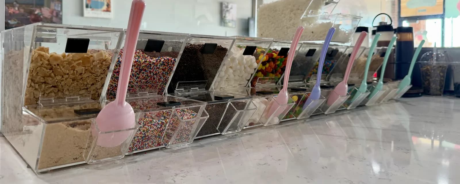 Palé's toppings bar: a long row of clear tubs along the marble counter, filled with rainbow sprinkles, crushed cookies, chocolate, mini marshmallows and candy, each with its own pastel scoop